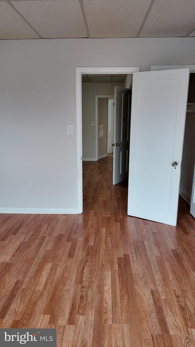 spare room with a drop ceiling, baseboards, and wood finished floors