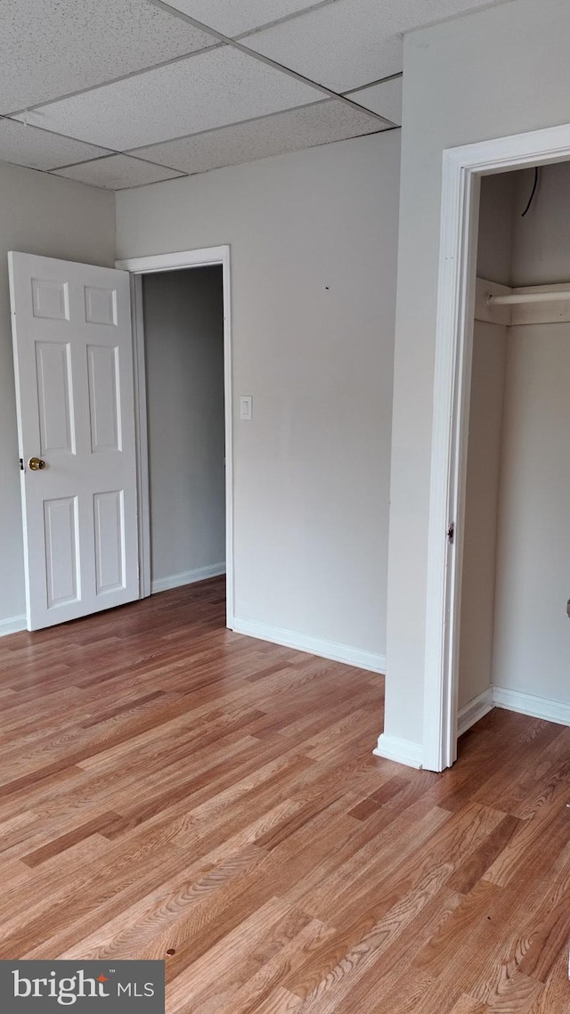 unfurnished bedroom with a drop ceiling, a closet, light wood-type flooring, and baseboards