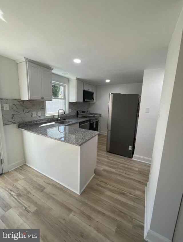 kitchen featuring tasteful backsplash, appliances with stainless steel finishes, light wood-style floors, a sink, and a peninsula