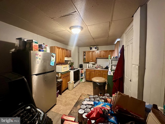 kitchen with brown cabinetry, range with gas stovetop, white microwave, freestanding refrigerator, and a paneled ceiling