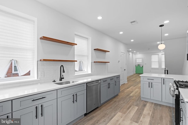 kitchen with decorative light fixtures, open shelves, light countertops, appliances with stainless steel finishes, and a sink