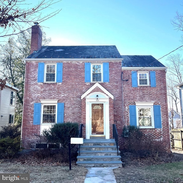 view of front facade with entry steps, a chimney, and brick siding