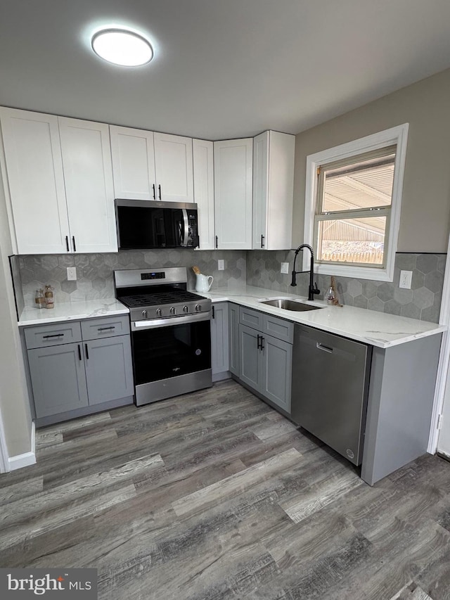 kitchen featuring appliances with stainless steel finishes, wood finished floors, light countertops, gray cabinetry, and a sink