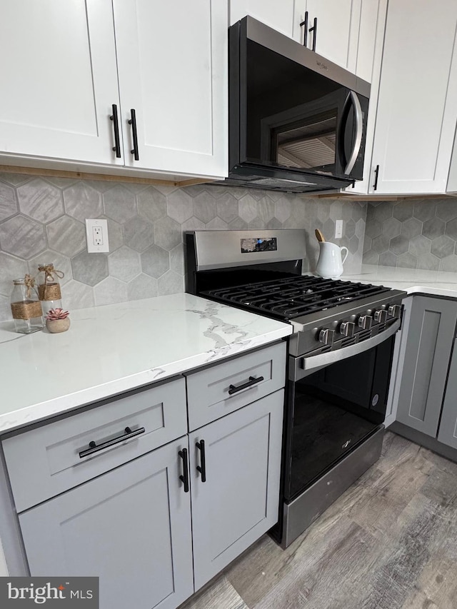 kitchen featuring appliances with stainless steel finishes, white cabinets, light wood-style floors, and decorative backsplash