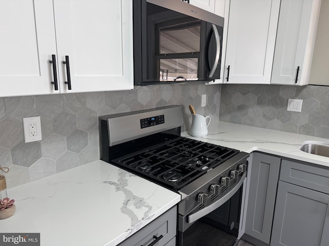 kitchen with light stone countertops, stainless steel range with gas cooktop, white cabinetry, and gray cabinetry