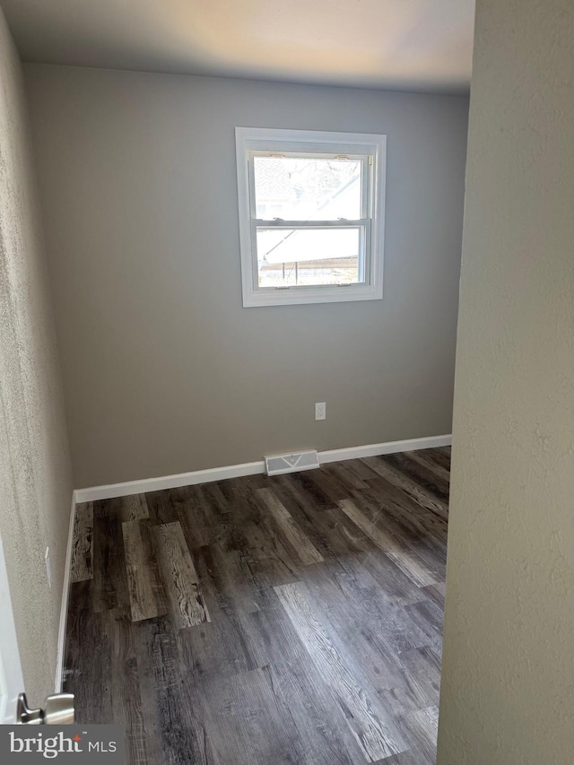 spare room with dark wood finished floors, visible vents, and baseboards