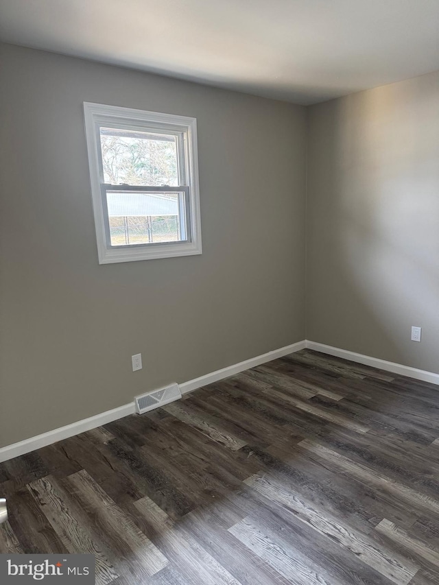 spare room featuring dark wood-style floors, visible vents, and baseboards