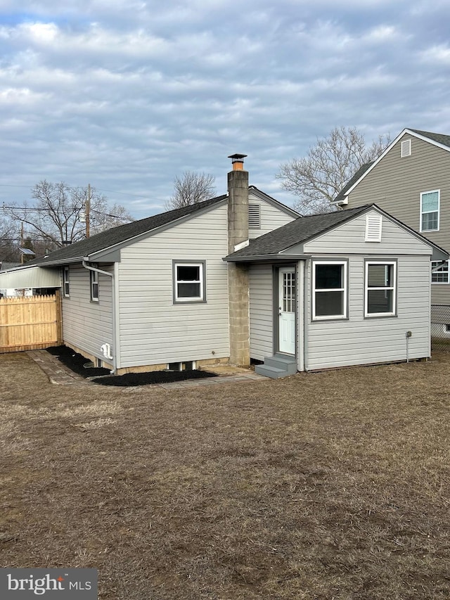 rear view of house featuring roof with shingles, a yard, a chimney, entry steps, and fence