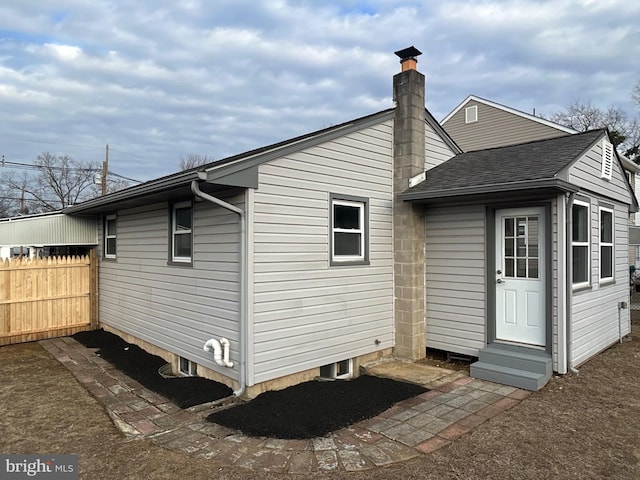 back of house with entry steps, a shingled roof, a chimney, and fence