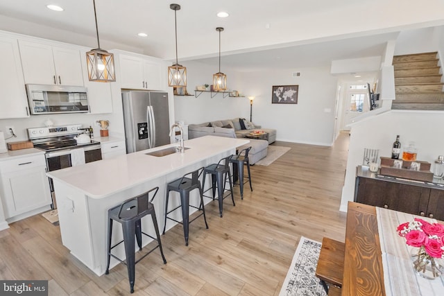 kitchen with a breakfast bar area, stainless steel appliances, a sink, white cabinetry, and light wood-style floors