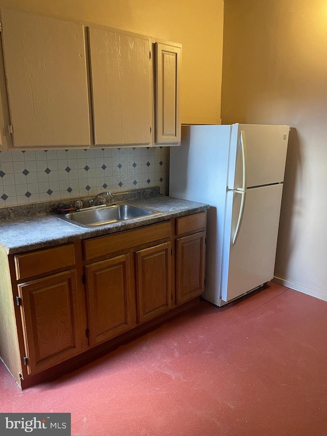 kitchen featuring dark countertops, backsplash, a sink, and freestanding refrigerator