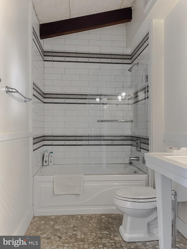 bathroom with wainscoting, shower / tub combination, and toilet