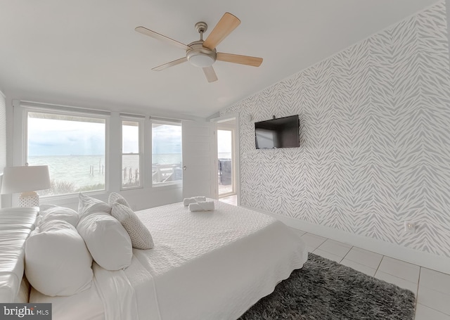 tiled bedroom with a ceiling fan, a water view, vaulted ceiling, and wallpapered walls