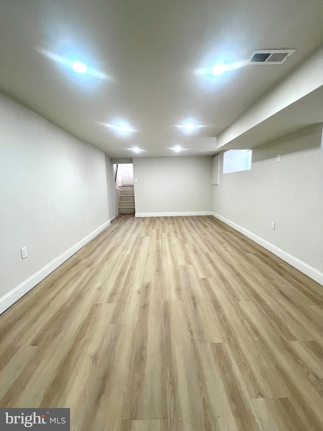 finished basement featuring light wood-type flooring, visible vents, stairway, and baseboards