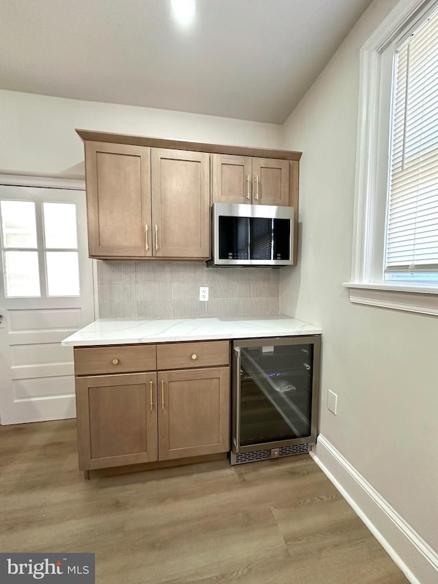 kitchen featuring light countertops, stainless steel microwave, backsplash, light wood-type flooring, and beverage cooler