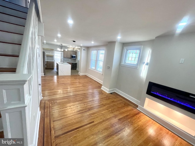 unfurnished living room featuring recessed lighting, a sink, wood finished floors, baseboards, and stairway