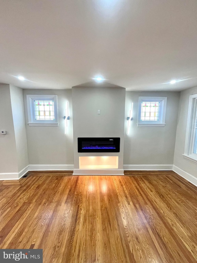 unfurnished living room with a glass covered fireplace, plenty of natural light, baseboards, and wood finished floors