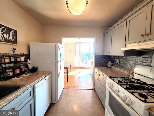 kitchen with decorative backsplash, gray cabinetry, a sink, white appliances, and under cabinet range hood