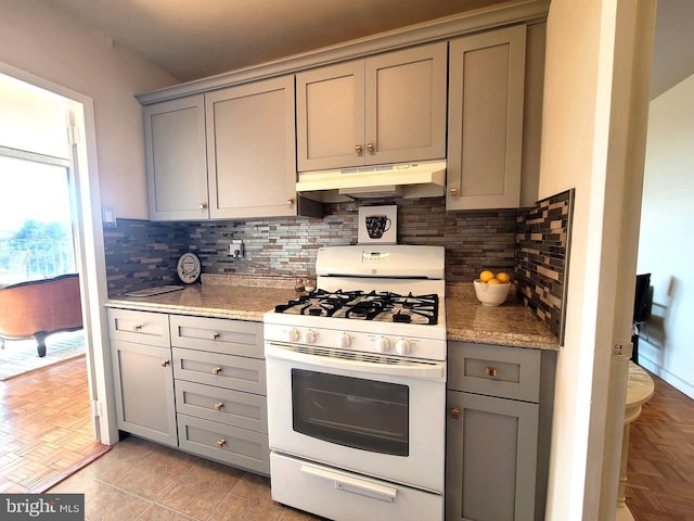 kitchen featuring gray cabinetry, white range with gas cooktop, decorative backsplash, and under cabinet range hood