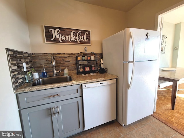 kitchen with light tile patterned floors, backsplash, gray cabinetry, a sink, and white appliances