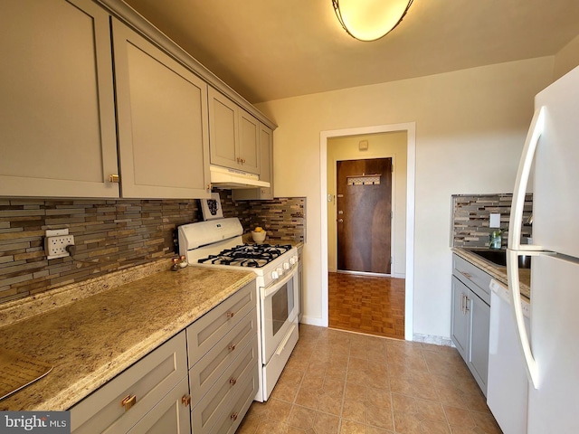 kitchen with light tile patterned floors, under cabinet range hood, white appliances, gray cabinets, and decorative backsplash