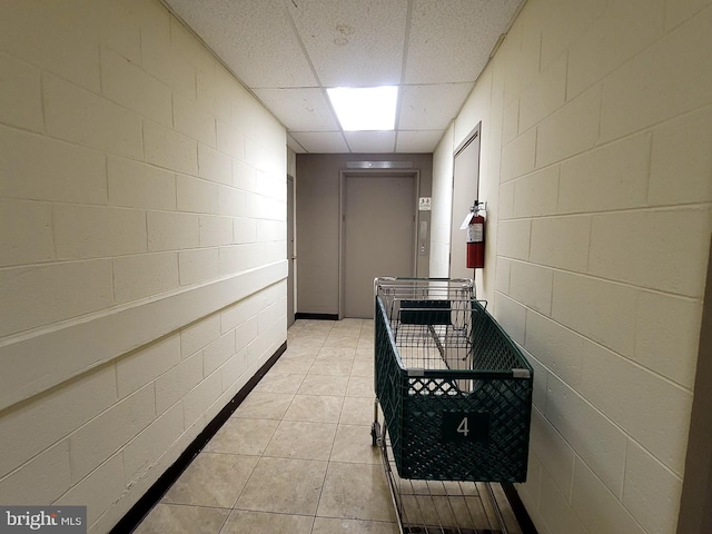 hall featuring concrete block wall, a drop ceiling, and light tile patterned flooring