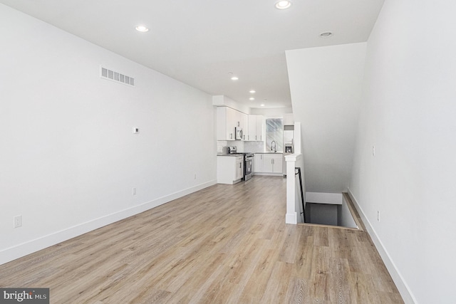 unfurnished living room featuring baseboards, visible vents, recessed lighting, a sink, and light wood-type flooring