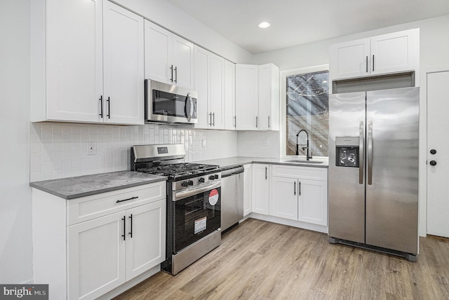 kitchen with appliances with stainless steel finishes, white cabinetry, light wood-style floors, and a sink