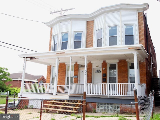 view of front of house featuring fence, a porch, and brick siding