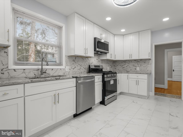 kitchen featuring marble finish floor, stainless steel appliances, a sink, and white cabinetry