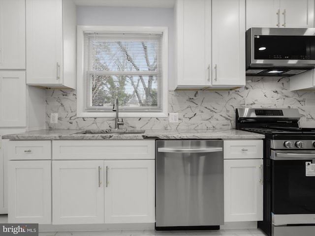 kitchen with tasteful backsplash, white cabinets, light stone counters, stainless steel appliances, and a sink