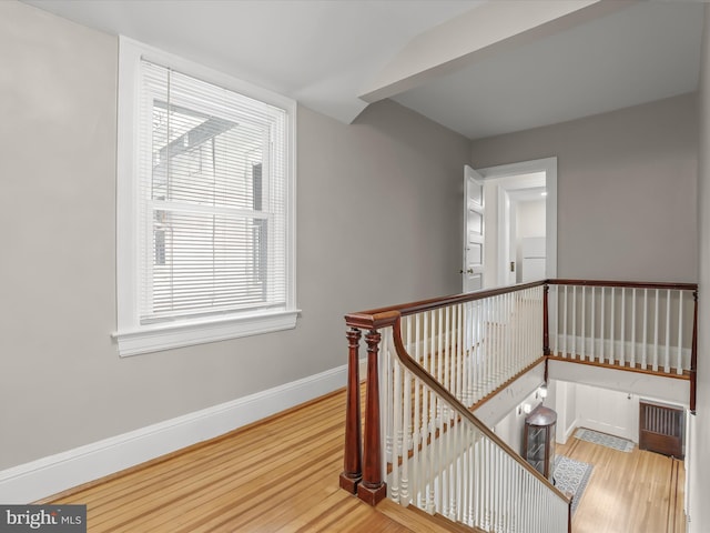 corridor with baseboards, wood finished floors, and an upstairs landing