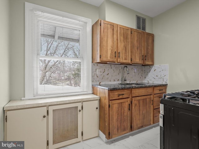 kitchen featuring a sink, marble finish floor, decorative backsplash, dark stone countertops, and gas range