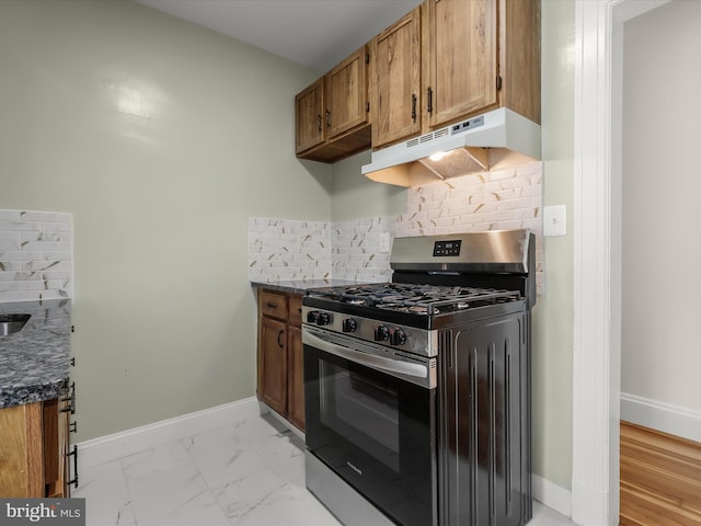 kitchen with marble finish floor, backsplash, stainless steel gas stove, under cabinet range hood, and baseboards