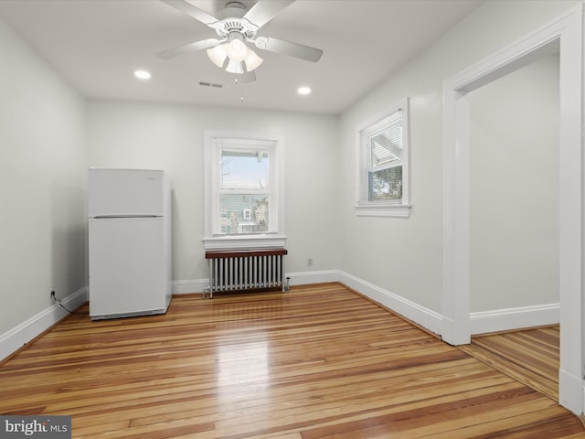 spare room featuring light wood finished floors, radiator heating unit, visible vents, and baseboards