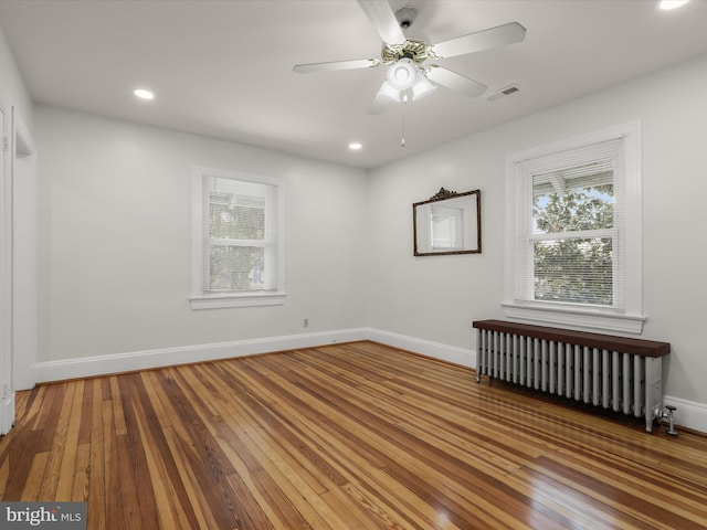 empty room featuring hardwood / wood-style flooring, radiator heating unit, baseboards, and recessed lighting