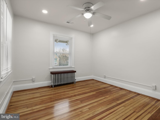 empty room featuring radiator heating unit, visible vents, wood-type flooring, and baseboards