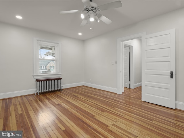 spare room with baseboards, light wood finished floors, and radiator