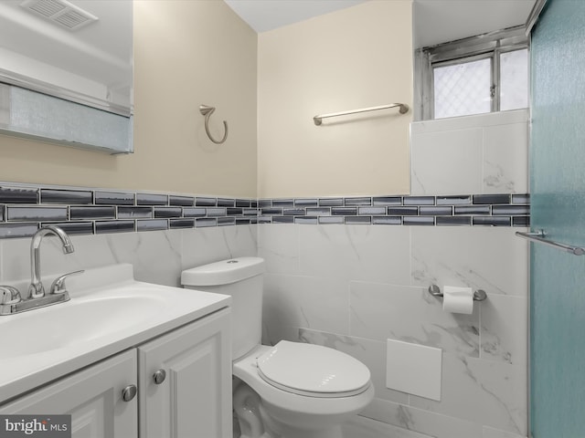 bathroom with visible vents, tile walls, toilet, and vanity