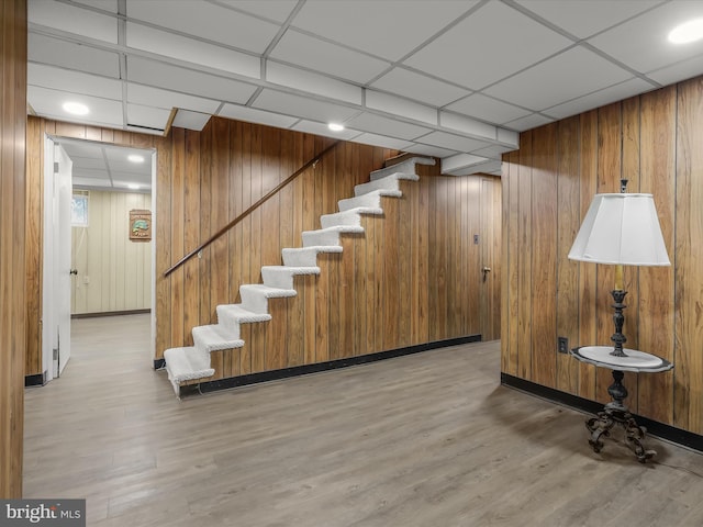 stairs featuring wood finished floors, a paneled ceiling, and wooden walls