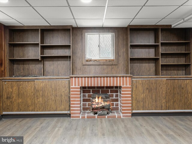 unfurnished living room with a paneled ceiling, a brick fireplace, and wood finished floors