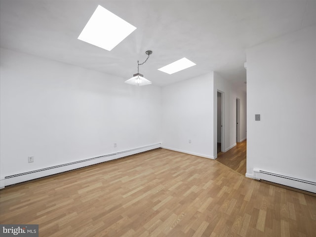 empty room featuring a baseboard heating unit, light wood finished floors, and a skylight