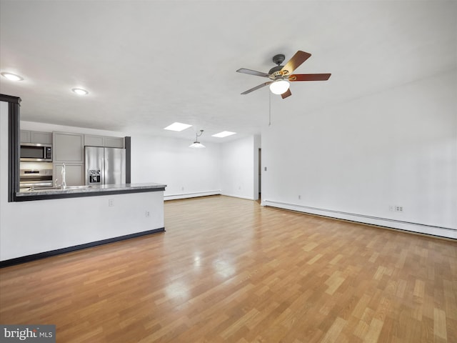 unfurnished living room featuring a baseboard heating unit, ceiling fan, and light wood-type flooring