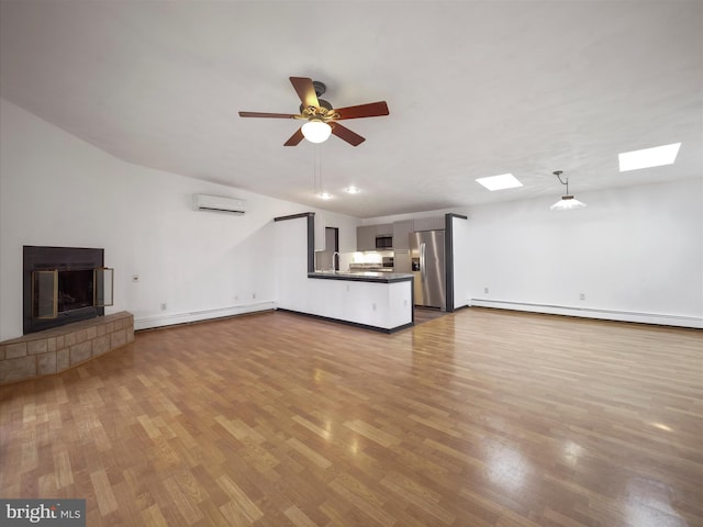 unfurnished living room with a tiled fireplace, baseboard heating, a wall unit AC, and wood finished floors