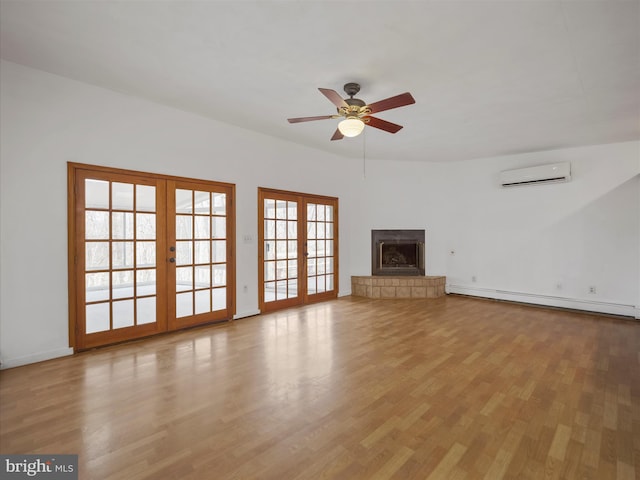 unfurnished living room featuring a baseboard radiator, light wood-style flooring, a wall mounted air conditioner, french doors, and a tiled fireplace