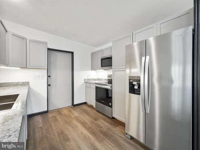 kitchen with appliances with stainless steel finishes, wood finished floors, gray cabinets, light countertops, and a sink