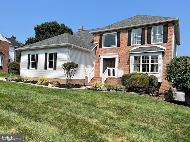 view of front facade with brick siding, roof with shingles, and a front yard