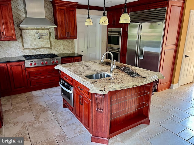 kitchen with appliances with stainless steel finishes, light stone counters, dark brown cabinets, wall chimney range hood, and a sink