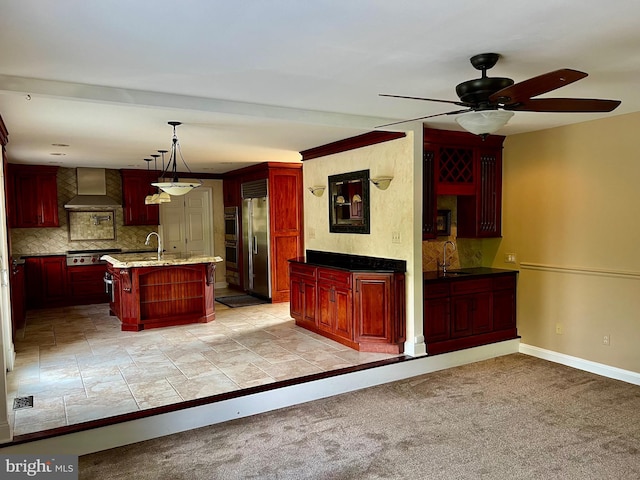 kitchen featuring tasteful backsplash, wall chimney exhaust hood, hanging light fixtures, a kitchen island with sink, and stainless steel appliances