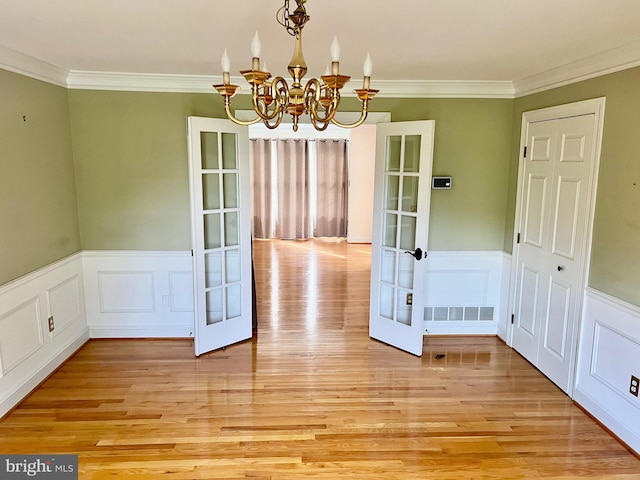 unfurnished dining area with a chandelier, light wood-style flooring, visible vents, ornamental molding, and french doors